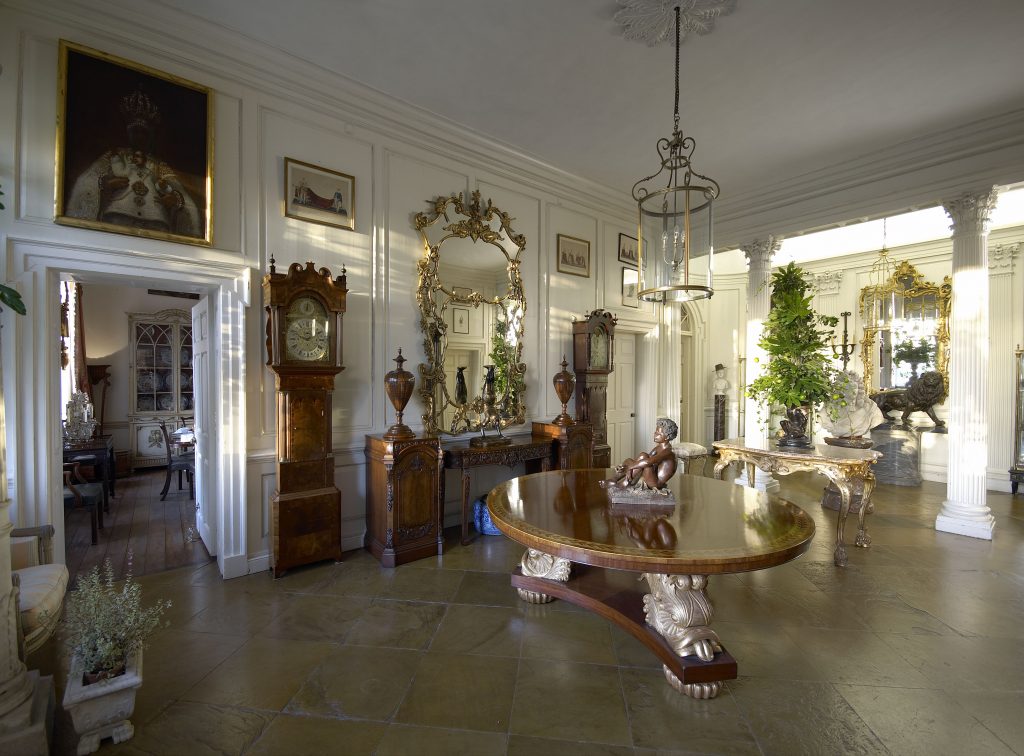 A photograph of a luxurious room featuring antique decorative items such as chandeliers, furniture, mirrors, fine art, and clocks.