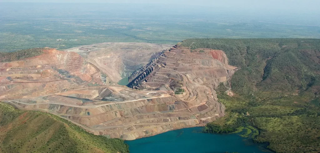 An aerial photograph of the Argyle Diamond mine. The photo shows a green landscape, with the center focused on a brown patch of land featuring mining equipment.