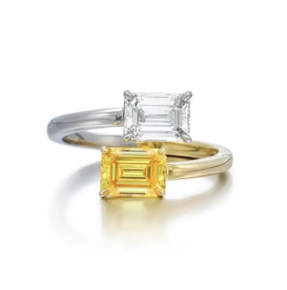 A photograph of a set with two emerald-cut diamonds. One is fancy vivid yellow, and the other is colorless. The ring is forged half Platinum and 18 karat gold in size 5¾.