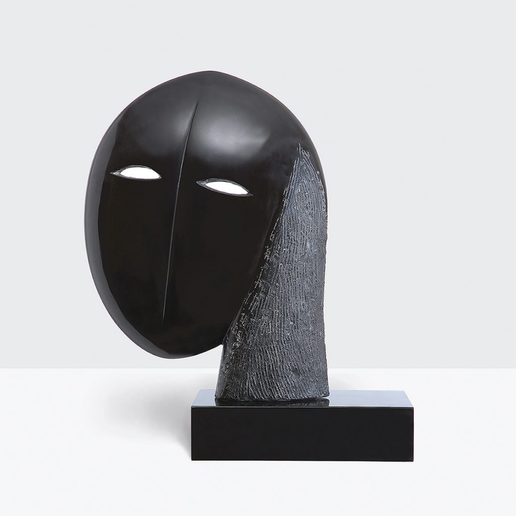 Joel Elenberg's Mask 1, 1978, depicts Elenberg’s then wife, Anna Schwartz, in marble. The sculpture appears to be an abstract head and on made of smooth dark stone set on a black block against a white background.