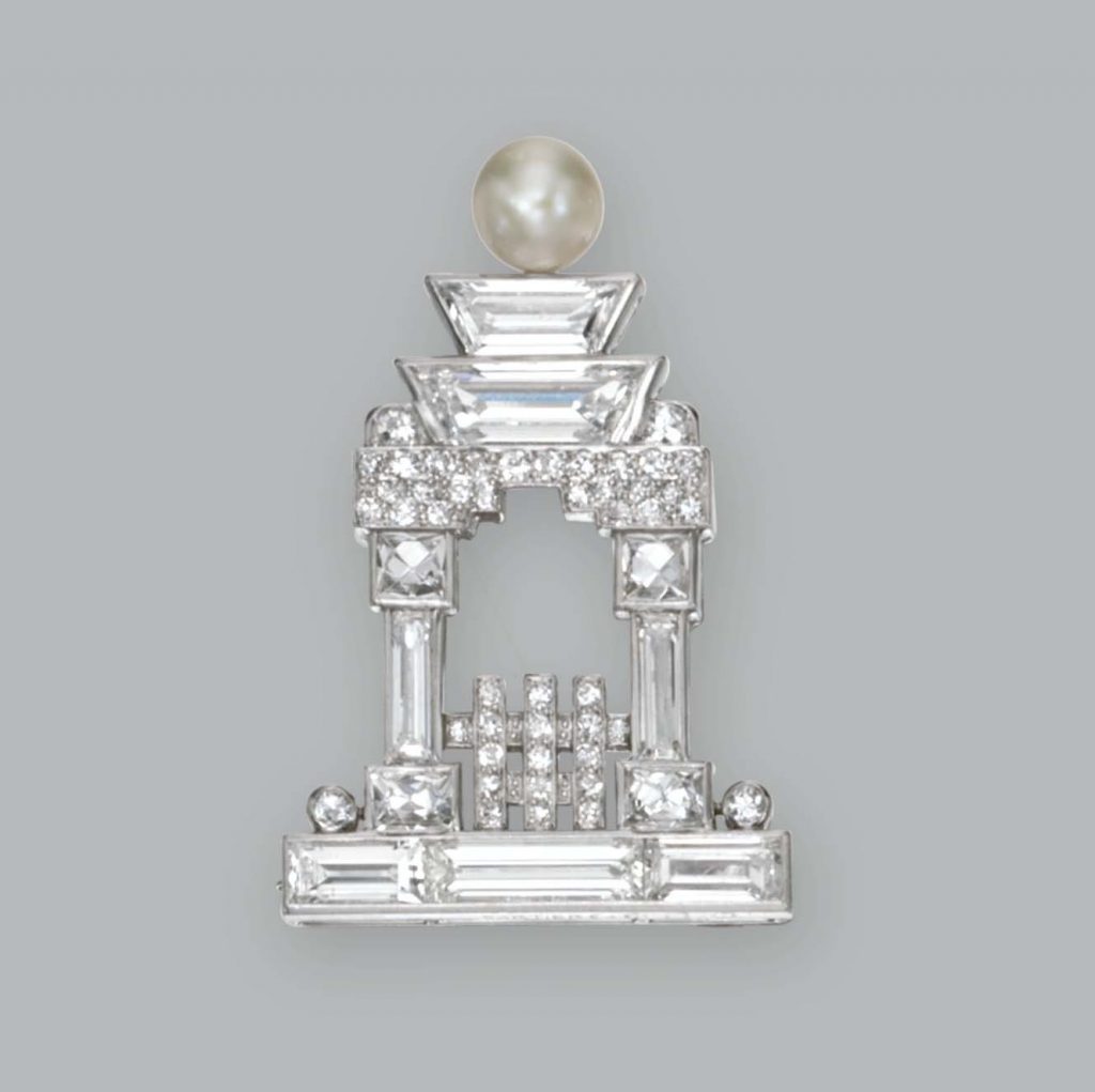 A small, diamond Cartier brooch in the shape of a pagoda against a grey studio background.